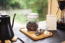 Nahaufnahme von Kaffeekanne, Glas mit Kaffeebohnen und Metallschaufel auf Holzbrett. — Stockfoto