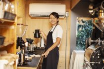 Японская женщина в фартуке, стоящая в эко-кафе, готовит кофе, улыбается в камеру
. — стоковое фото