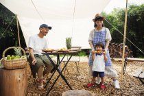 Hombre, mujer y niño japoneses se reunieron alrededor de una mesa bajo un dosel, preparando verduras . - foto de stock