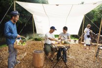 Gruppo di uomini, donne e bambini giapponesi riuniti attorno a un tavolo sotto un baldacchino, che preparano verdure . — Foto stock