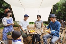 Group of Japanese men and women with child gathered around a table under a canopy, preparing vegetables. — Stock Photo