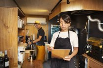 Japanese woman and man working in an Eco Cafe, preparing coffee, using mobile phone. — Stock Photo
