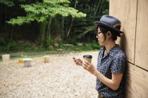 Japanese woman in glasses and hat standing outside Eco Cafe, holding paper cup. — Stock Photo