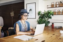 Female Japanese professional sitting at a table in a co-working space, using laptop computer. — Stock Photo