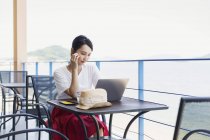 Female Japanese professional sitting on balcony of a co-working space, using laptop computer. — Stock Photo