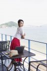 Японская женщина-профессионал, стоящая на балконе коворкинга, ноутбук на столе . — стоковое фото