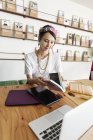 Mujer japonesa profesional sentada a la mesa en un espacio de co-trabajo, utilizando tableta digital y portátil, libro de celebración
. - foto de stock