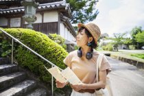 Mulher japonesa usando chapéu e segurando mapa em pé fora do templo budista . — Fotografia de Stock