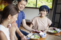 Camarero sirviendo a dos mujeres japonesas sentadas en una mesa en un restaurante japonés . - foto de stock