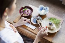 Vista de ángulo alto de la mujer japonesa sentada en una mesa en un restaurante japonés, comiendo . - foto de stock