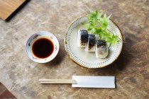 High angle close-up of plate of sushi and bowl of soy sauce on a table in Japanese restaurant. — Stock Photo