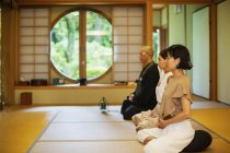 Two Japanese women and Buddhist priest kneeling in Buddhist temple, praying. — Stock Photo