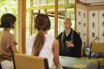 Two women and Buddhist priest kneeling in Buddhist temple, talking. — Stock Photo