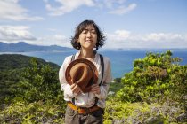 Japanese woman holding hat standing on a cliff with ocean scenery. — Stock Photo