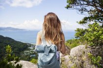 Вид сзади женщины с рюкзаком, стоящей на скалах на скале с океанскими пейзажами
. — стоковое фото