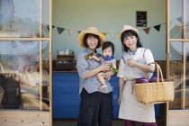Zwei japanische Frauen und ein Junge stehen vor einem Hofladen und lächeln in die Kamera. — Stockfoto