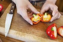 High angle close-up of person cutting fresh red bell peppers on wooden cutting board. — Stock Photo