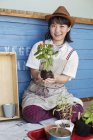 Japanese woman sitting outside a farm shop, planting flowers into flower pots. — Stock Photo