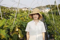 Japanerin mit Hut steht auf Gemüsefeld und lächelt in die Kamera. — Stockfoto