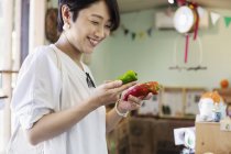 Sorridente donna giapponese in piedi in un negozio di fattoria, con in mano peperoni biologici . — Foto stock