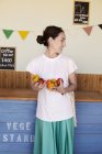 Sorridente donna giapponese in piedi in un negozio di fattoria, con verdure in mano . — Foto stock