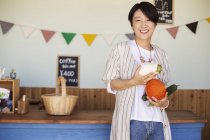 Donna giapponese in piedi in un negozio di fattoria, con le verdure in mano, sorridente in macchina fotografica . — Foto stock