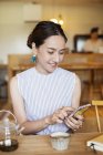 Femme japonaise assise à une table dans un café végétarien, en utilisant un téléphone portable . — Photo de stock
