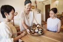 Proprietário japonês servindo clientes femininos em um café vegetariano . — Fotografia de Stock