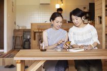 Zwei japanische Frauen sitzen an einem Tisch in einem vegetarischen Café und benutzen ein Mobiltelefon. — Stockfoto