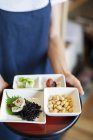 High angle close-up of waitress holding a selection of vegetarian Japanese food plates in a cafe. — Stock Photo