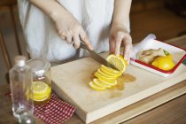 Primo piano ad angolo alto di persona che taglia fette di limone con coltello sul tagliere di legno
. — Foto stock
