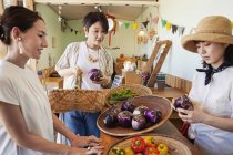 Japanese woman in hat working in a farm shop, serving female customers. — Stock Photo