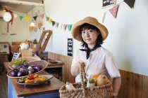 Japonesa mujer en sombrero trabajando en una granja tienda, sonriendo en cámara . - foto de stock
