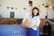 Japanese woman in hat working in a farm shop, smiling in camera. — Stock Photo