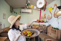 Japanerin mit Hut arbeitet in einem Hofladen und wiegt frische Paprika. — Stockfoto