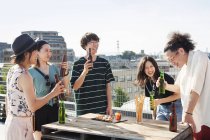 Группа молодых японских мужчин и женщин, стоящих на крыше в городской обстановке, пьющих пиво с закусками . — стоковое фото