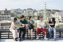 Grupo de jóvenes japoneses sentados en la azotea en un entorno urbano, bebiendo cerveza . - foto de stock