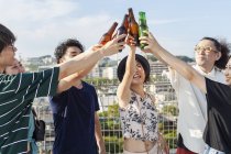 Gruppo di giovani giapponesi uomini e donne in piedi sul tetto in ambiente urbano, brindare bottiglie di birra . — Foto stock