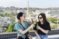 Two young Japanese women sitting on rooftop in urban setting, drinking beer. — Stock Photo