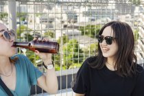 Due giovani donne giapponesi sedute sul tetto in ambiente urbano, a bere birra . — Foto stock