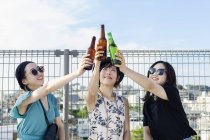 Junge japanische Frauen sitzen auf einem Dach in urbaner Umgebung und prosten Bier zu. — Stockfoto