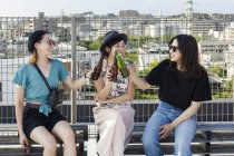 Троє молодих японських жінок сидять на даху в місті і п 