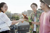 Молодые японские мужчины и женщины стоят на крыше в городской обстановке, пьют пиво . — стоковое фото