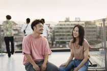 Sonriente joven japonés hombre y mujer sentado en la azotea en el entorno urbano
. - foto de stock