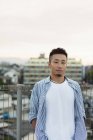 Молодий японець стоїть на даху в місті і дивиться в камеру.. — стокове фото