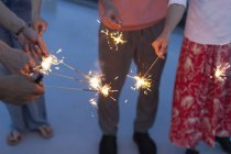 Hands of men and women with sparklers on rooftop. — Stock Photo