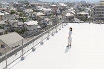 High angle view of young Japanese woman standing on rooftop in urban setting. — Stock Photo