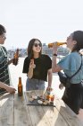 Young Japanese man and women standing on rooftop in urban setting, drinking beer with snacks. — Stock Photo