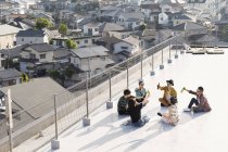 Высокий угол обзора группы молодых японских мужчин и женщин, сидящих на крыше в городской обстановке
. — стоковое фото
