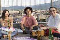 Smiling group of young Japanese men and woman sitting on rooftop in urban setting. — Stock Photo